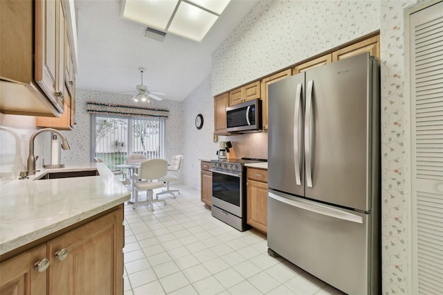 kitchen featuring stainless steel appliances, sink, vaulted ceiling, light stone counters, and ceiling fan