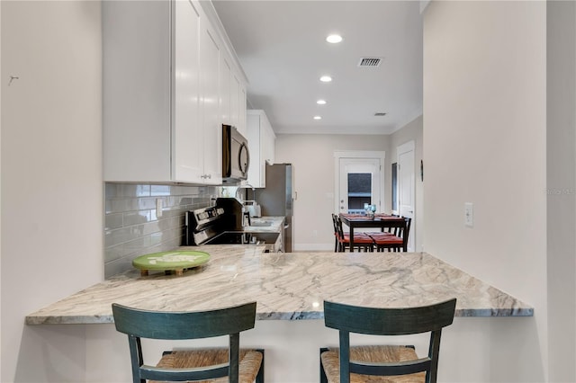 kitchen featuring appliances with stainless steel finishes, white cabinets, a kitchen bar, and light stone counters