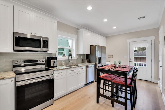 kitchen with appliances with stainless steel finishes, light stone counters, plenty of natural light, sink, and white cabinetry