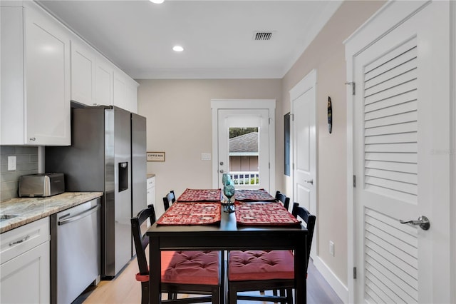 kitchen with light hardwood / wood-style floors, light stone countertops, white cabinets, stainless steel dishwasher, and backsplash