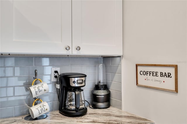 interior details with white cabinets, decorative backsplash, and light stone countertops