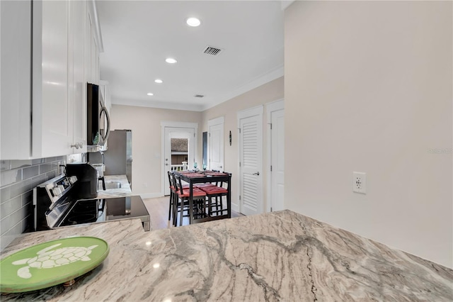 kitchen with stainless steel appliances, white cabinets, light stone counters, hardwood / wood-style floors, and crown molding