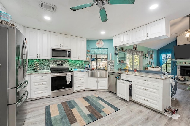 kitchen featuring kitchen peninsula, appliances with stainless steel finishes, vaulted ceiling, white cabinets, and sink