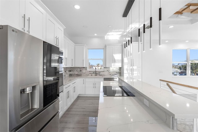 kitchen featuring stainless steel fridge with ice dispenser, white cabinetry, light stone countertops, pendant lighting, and sink