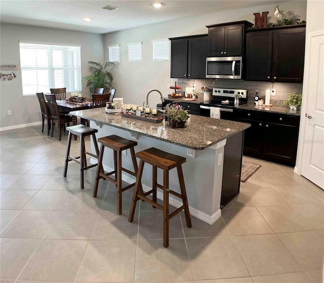 kitchen featuring a breakfast bar, stainless steel appliances, an island with sink, and light tile patterned floors