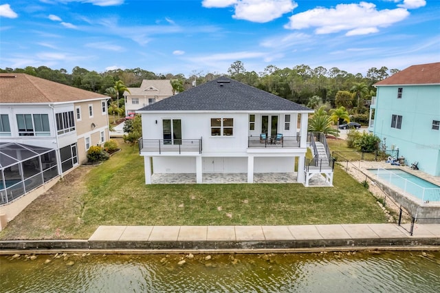 back of house featuring a water view, a balcony, and a lawn