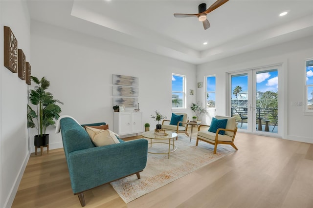 living room featuring ceiling fan, a raised ceiling, and light hardwood / wood-style floors