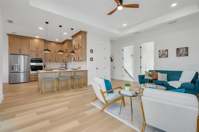 living room with a raised ceiling, ceiling fan, and light wood-type flooring