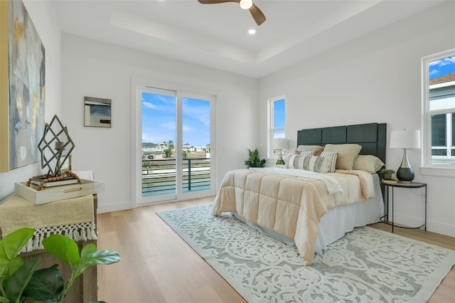 bedroom with access to exterior, light hardwood / wood-style floors, a raised ceiling, and ceiling fan