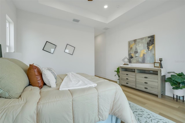 bedroom with a raised ceiling and light hardwood / wood-style floors