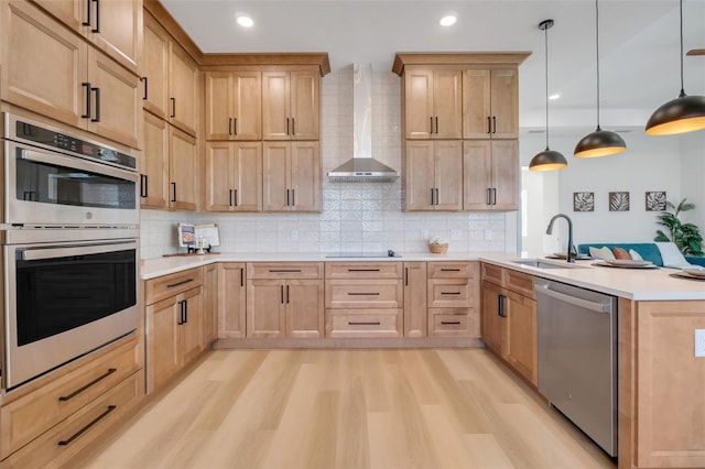 kitchen featuring light brown cabinetry, sink, hanging light fixtures, stainless steel appliances, and wall chimney exhaust hood