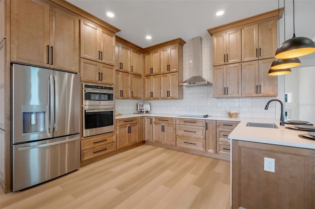 kitchen with wall chimney exhaust hood, sink, decorative light fixtures, light hardwood / wood-style flooring, and stainless steel appliances