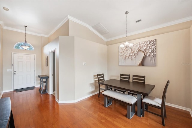 dining space with crown molding, hardwood / wood-style flooring, vaulted ceiling, and a notable chandelier