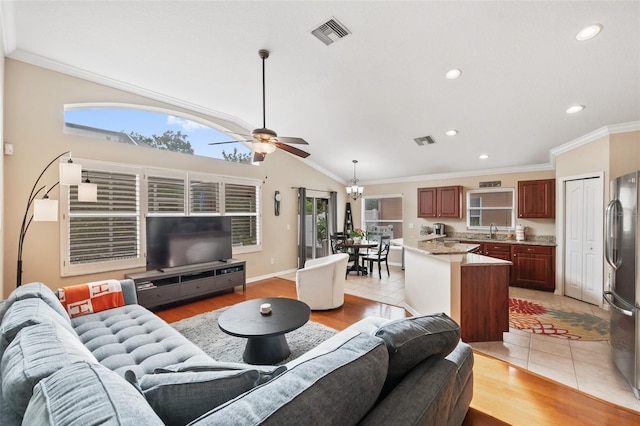 living room with crown molding, light tile patterned floors, sink, ceiling fan with notable chandelier, and lofted ceiling