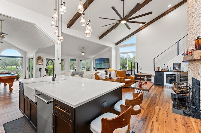 kitchen with wine cooler, beamed ceiling, a stone fireplace, and light hardwood / wood-style floors