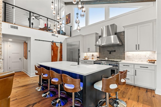 kitchen featuring tasteful backsplash, pendant lighting, high end appliances, white cabinetry, and wall chimney exhaust hood