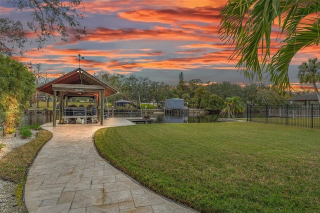 surrounding community with a water view, a boat dock, and a lawn