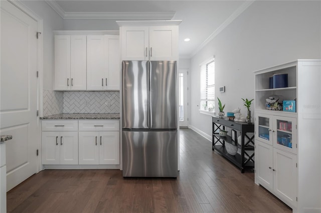 kitchen with white cabinetry, light stone counters, ornamental molding, stainless steel refrigerator, and backsplash