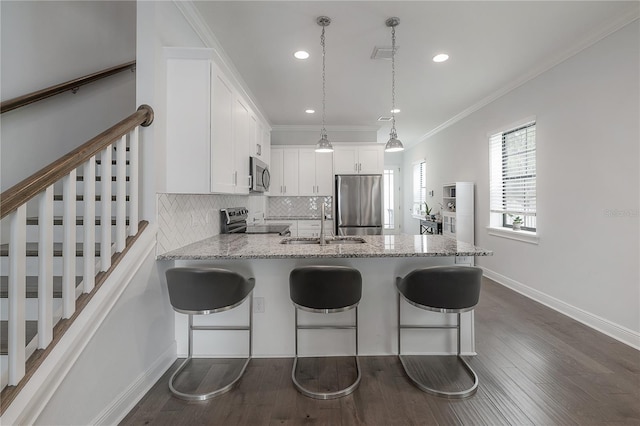 kitchen with appliances with stainless steel finishes, kitchen peninsula, a kitchen bar, white cabinets, and decorative light fixtures