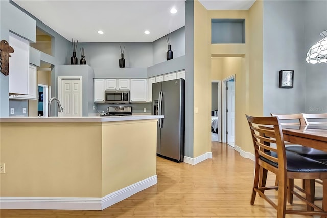 kitchen featuring a high ceiling, appliances with stainless steel finishes, light wood-type flooring, white cabinets, and sink