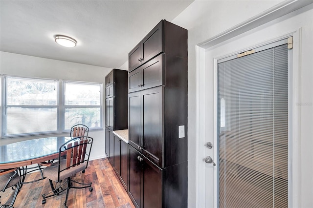 kitchen with dark brown cabinets, light hardwood / wood-style flooring, and light stone counters