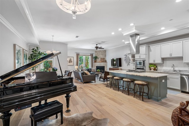 interior space featuring light hardwood / wood-style flooring, sink, crown molding, ceiling fan, and a stone fireplace