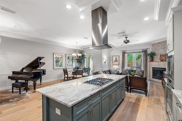 kitchen with island exhaust hood, stainless steel appliances, a center island, white cabinetry, and ceiling fan with notable chandelier