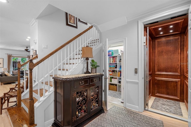 staircase featuring wood-type flooring, ceiling fan, and ornamental molding