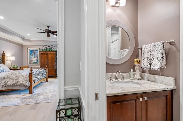 bathroom featuring a raised ceiling, wood-type flooring, crown molding, vanity, and ceiling fan