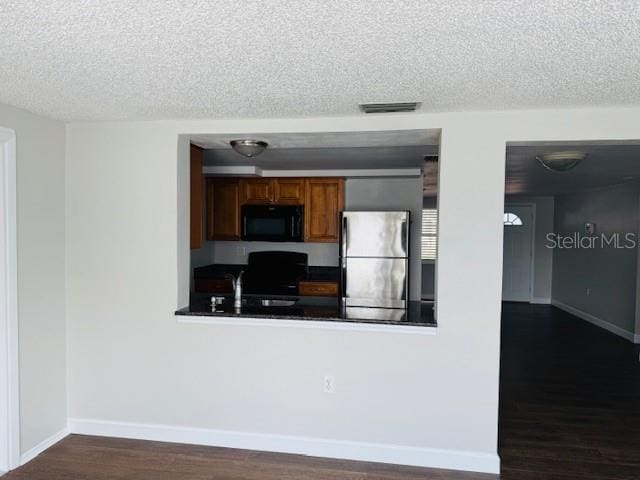 kitchen with dark wood-type flooring, stainless steel fridge, sink, and a textured ceiling