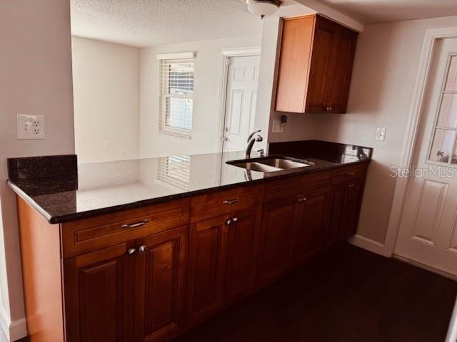 kitchen with sink, a textured ceiling, kitchen peninsula, and dark stone counters