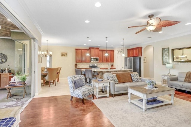 living room with crown molding, ceiling fan with notable chandelier, and light hardwood / wood-style flooring