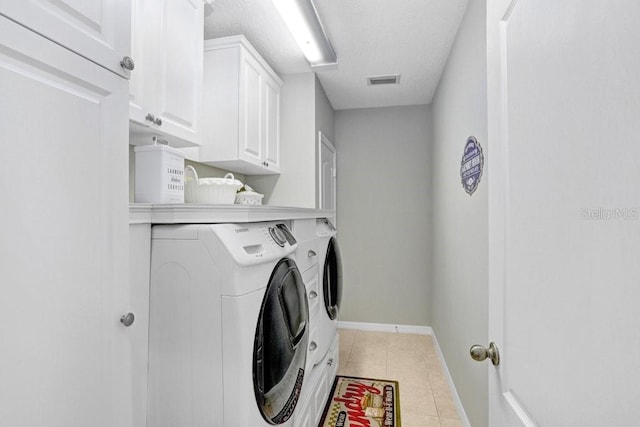 laundry area with light tile patterned flooring, separate washer and dryer, a textured ceiling, and cabinets