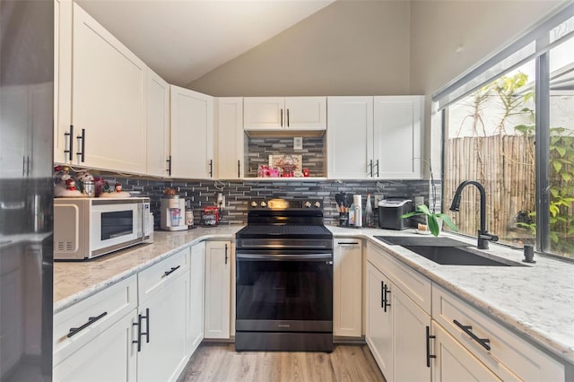 kitchen with sink, white cabinets, light stone counters, lofted ceiling, and black / electric stove