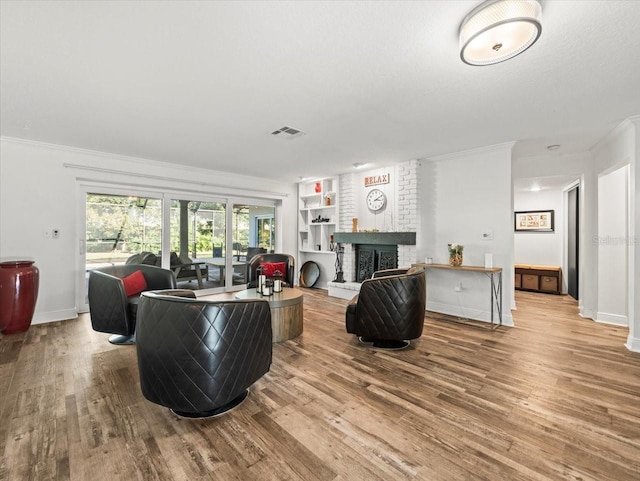 living room featuring hardwood / wood-style flooring, a textured ceiling, built in shelves, crown molding, and a fireplace