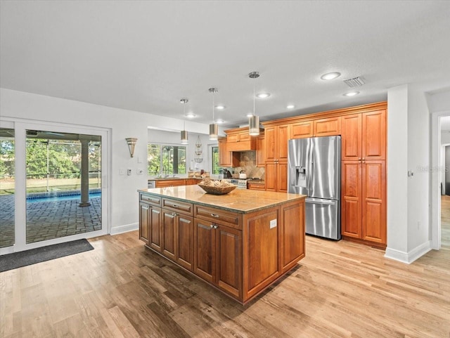 kitchen with light hardwood / wood-style floors, stainless steel appliances, decorative light fixtures, and a kitchen island