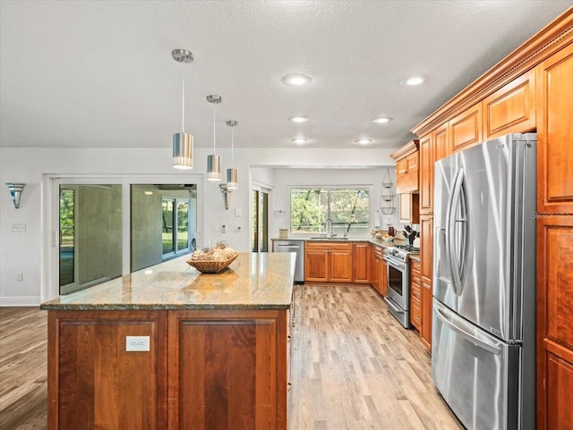 kitchen featuring light stone counters, decorative light fixtures, a kitchen island, light wood-type flooring, and appliances with stainless steel finishes