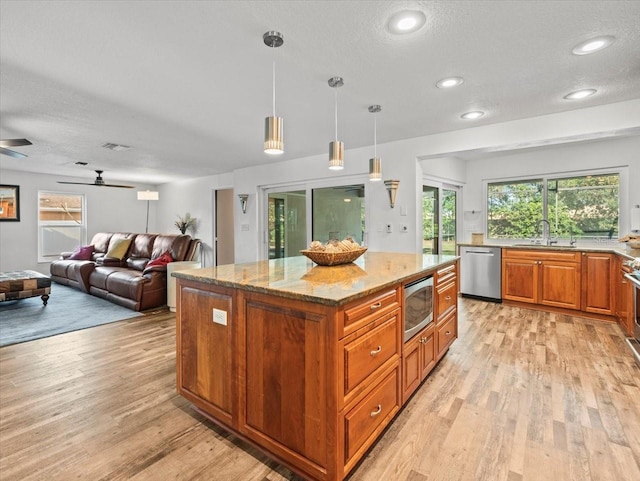 kitchen with sink, decorative light fixtures, light stone counters, a kitchen island, and appliances with stainless steel finishes