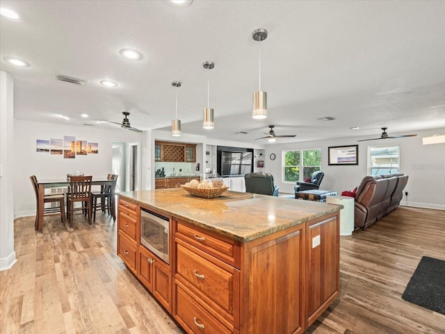 kitchen with stainless steel microwave, light stone countertops, light hardwood / wood-style flooring, a center island, and hanging light fixtures