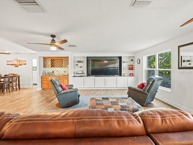 living room featuring built in shelves, ceiling fan, and light hardwood / wood-style flooring