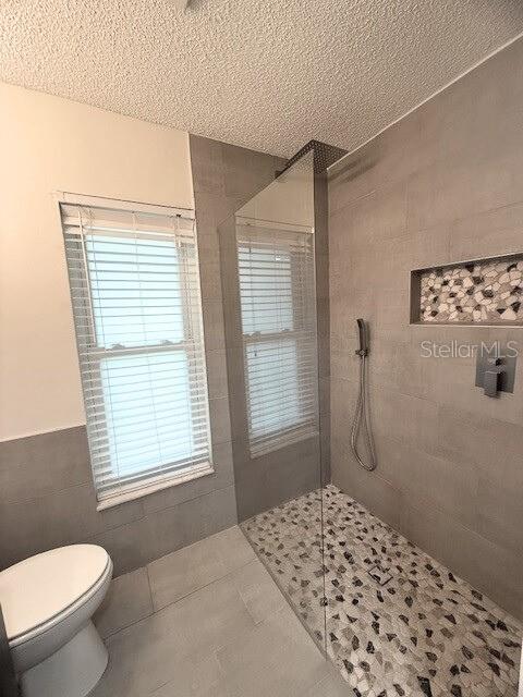 bathroom with a textured ceiling, a healthy amount of sunlight, and tile walls