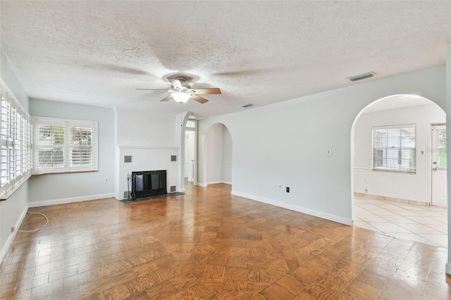 unfurnished living room featuring a fireplace, ceiling fan, and a healthy amount of sunlight