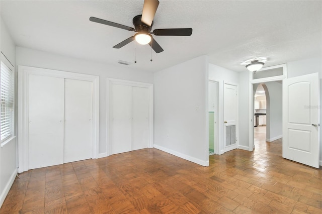 unfurnished bedroom featuring hardwood / wood-style flooring, a textured ceiling, ceiling fan, and multiple closets