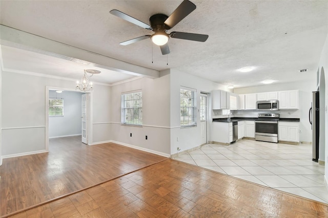 kitchen featuring stainless steel appliances, decorative light fixtures, white cabinetry, light tile patterned floors, and ceiling fan with notable chandelier