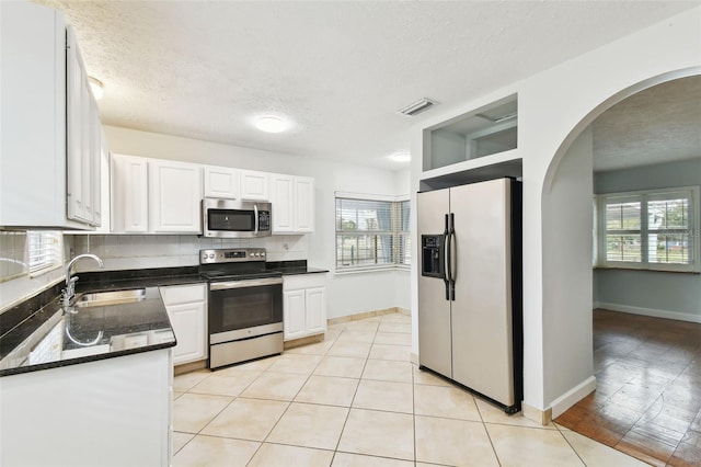 kitchen with appliances with stainless steel finishes, white cabinetry, light tile patterned floors, and sink