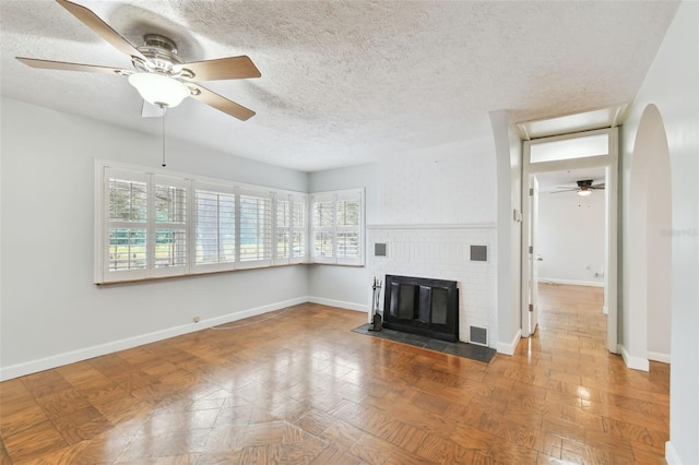 unfurnished living room with a brick fireplace, ceiling fan, and a wealth of natural light