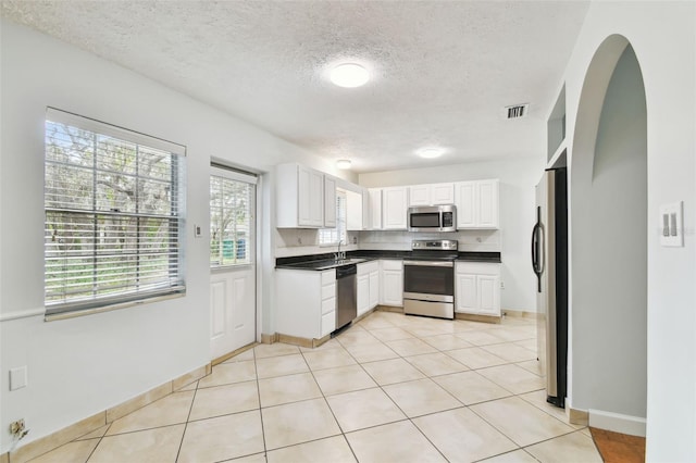 kitchen with appliances with stainless steel finishes, light tile patterned floors, a textured ceiling, white cabinets, and sink