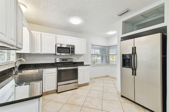 kitchen with appliances with stainless steel finishes, white cabinetry, light tile patterned floors, and sink