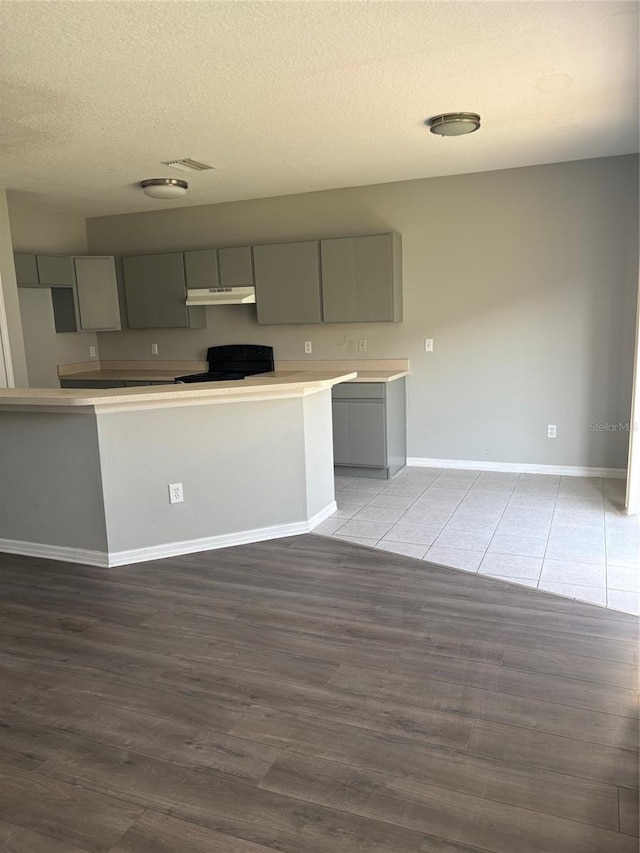 kitchen with a textured ceiling, electric range oven, gray cabinets, and dark hardwood / wood-style floors