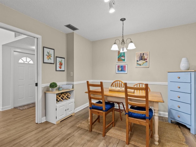 dining room with visible vents, light wood-style flooring, an inviting chandelier, a textured ceiling, and baseboards